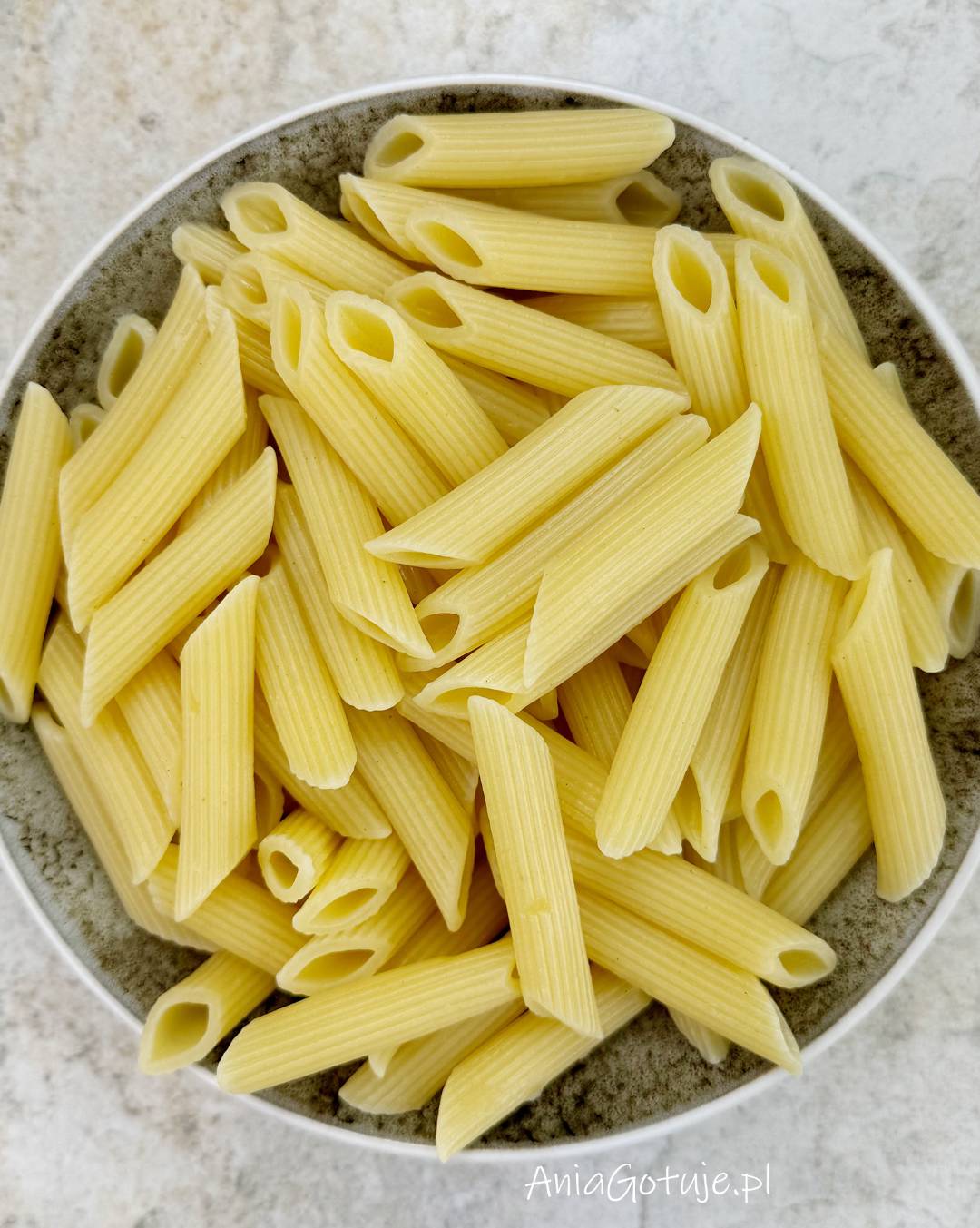 W głębokiej misce znajduje się porcja jasnożółtego makaronu penne, odcedzonego po gotowaniu al dente. Rurki są błyszczące i lekko wilgotne, gotowe do dodania do smażonych kurek.