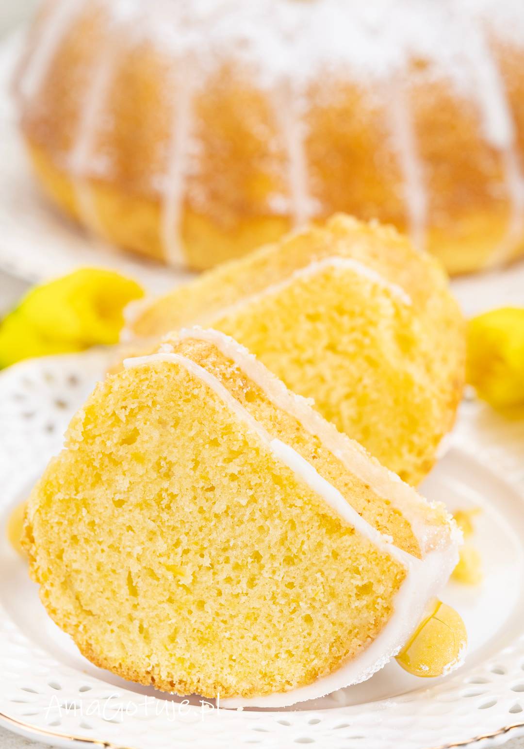Pokrojona babka została ujęta w dużym zbliżeniu, dzięki czemu dobrze widoczny jest jej jasny, drobny i równy miękisz. Na wierzchu kawałków znajduje się cienka warstwa białego lukru, a w tle występuje rozmyty fragment całej babki.