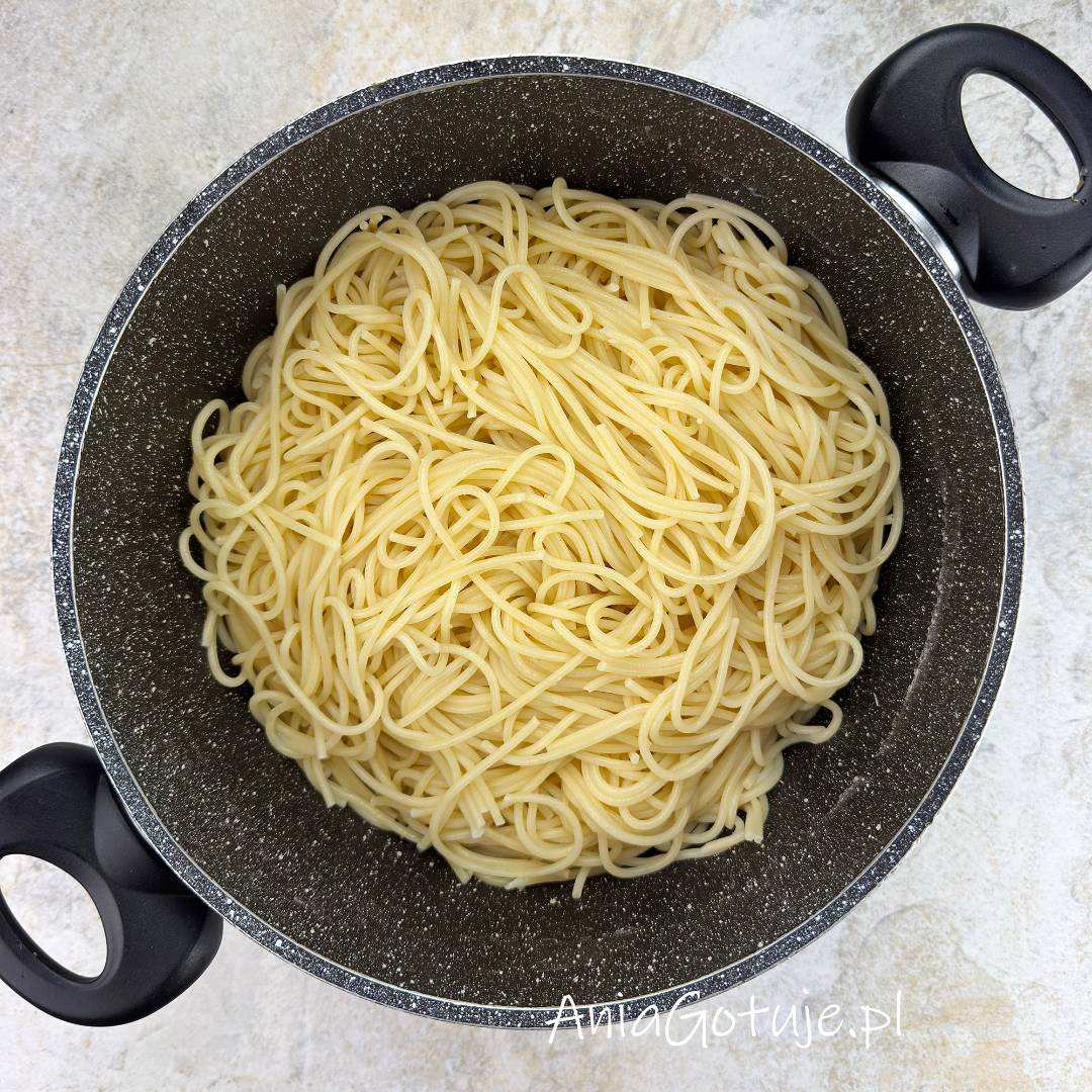W dużym garnku znajduje się porcja ugotowanego spaghetti o jasnym kolorze i gładkiej, sprężystej strukturze. Długie nitki zostały odcedzone i umieszczone z powrotem w naczyniu, gotowe do połączenia z sosem do spaghetti z mięsem mielonym.