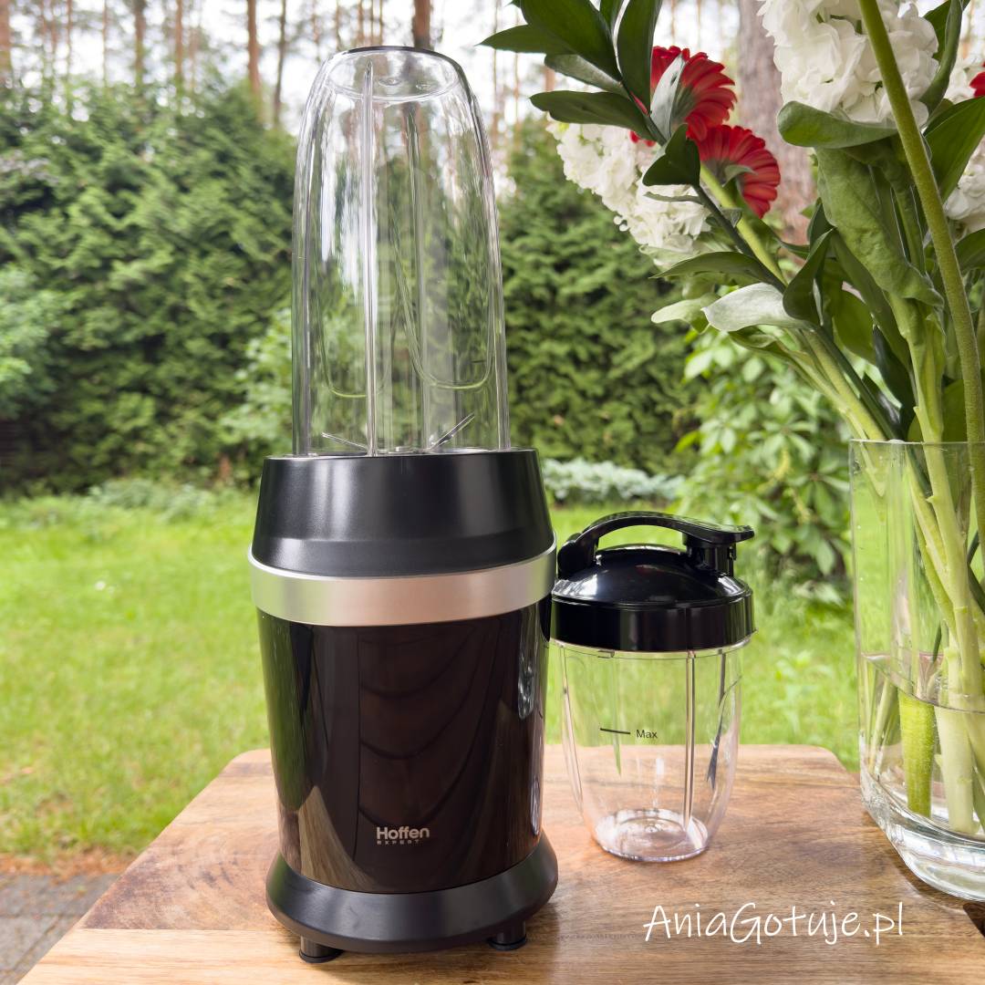 Blender fitness z pustą butelką do miksowania został ustawiony na drewnianym blacie, a obok umieszczono przezroczysty bidon z czarną pokrywką. To etap przygotowania sprzętu do zrobienia koktajlu odchudzającego przed dodaniem składników.